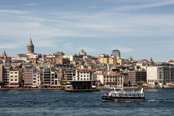 Fototapeta premium View of a tour boat on Golden Horn part of Bosphorus in Istanbul. Galata tower and Beyoglu district are in the view. It is a sunny summer day.