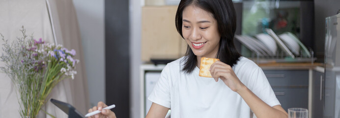 Asian woman eats breakfast with crackers (Healthy whole grain) and juice, Use your phone or tablet to search for morning news, Small room in condominium background, Wake-up activities..