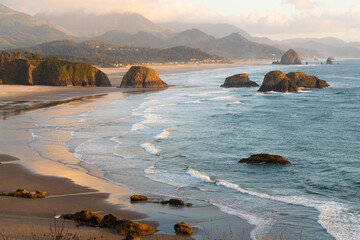 Late evening sunlight falls across Cannon Beach and the sea stacks on the Oregon Caost alongside the Pacific Ocean
