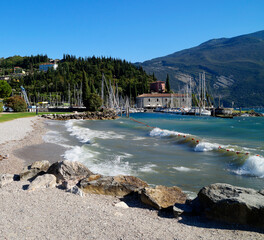 Fototapeta premium scenic beach line and harbor of the mediterranean town Riva del Garda on lake Garda with the mountains in the background in Lombardy, Italy