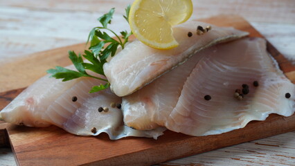 Fresh tilapia fish fillet sliced for steak or salad with herbs spices and lemon