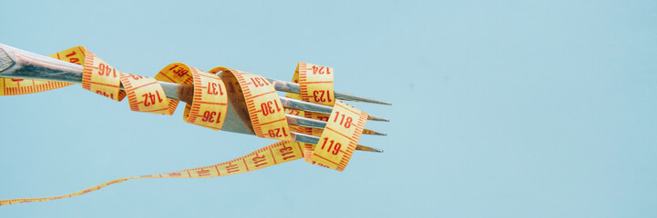 Bright yellow measuring tape on fork on a blue background. Diet concept. Banner