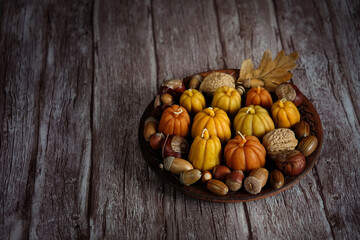 pumpkin shape candles, acorns and nuts on plate, dark wooden background. autumn seasonal composition. symbol of harvest, Mabon, thanksgiving holiday, Halloween. fall time. witch magic ritual
