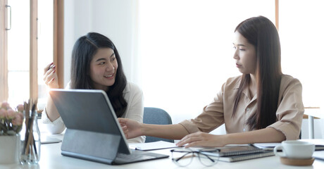 Obraz na płótnie Canvas Two young Asian businesswoman discuss investment project working and planning strategy. Business people talking together with laptop computer at office.