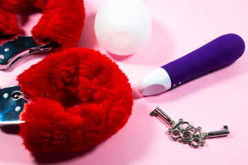 Red sexy fluffy handcuffs with keys and vibrator on a pink background. Erotic sex game with sexual bdsm toys.