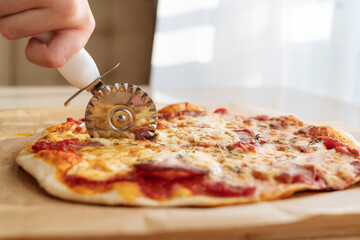 A hand with a pizza knife cuts a pizza close-up.