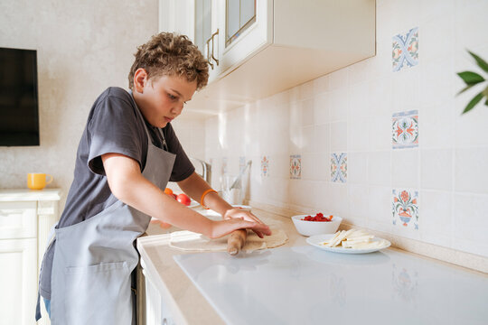 An 11-year-old boy rolls pizza dough in the kitchen.