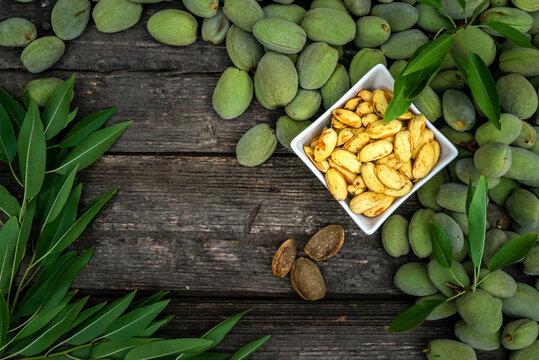 Green almonds open background   fresh raw unripe wooden rustic table blurred garden background leaves, Top view copy space shell  tree branch frame Peeled almond kernel milk husks white Bowl