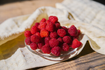 Raspberry fruits on a small saucer, a bunch of summer berries on a wooden background. Summer background. Juicy appetizer or dessert.