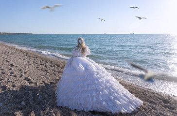 Young brunette woman in summer white dress standing on beach and looking to the sea.