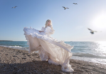 Young brunette woman in summer white dress standing on beach and looking to the sea.