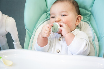 A happy and contented baby eats banana puree from a nipple. Introduction of complementary foods, healthy baby food, feeding the baby at the table