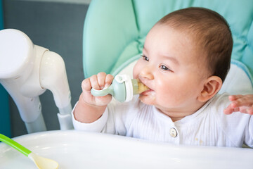 A happy and contented baby eats banana puree from a nipple. Introduction of complementary foods,...