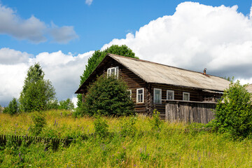 Rustic log old wooden house in village on hill on natural background of sky clouds grass trees