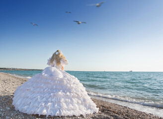 Young brunette woman in summer white dress standing on beach and looking to the sea.