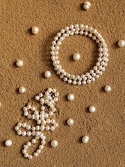 Pearl jewelry and pearl beads on the sand. A creative wedding concept with white necklace and a...