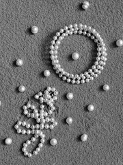 Pearl jewelry and pearl beads on the sand. A creative wedding concept with white necklace and a pearl bracelet. Summer background with pearls on the sand.