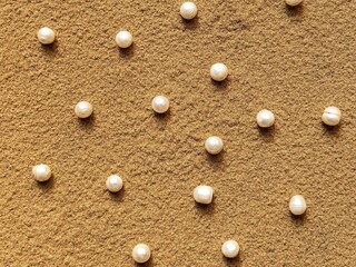 Fototapeta na wymiar Pearls pattern on the sand. A creative wedding concept with white pearl. Summer background with pearls on the sand.
