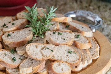 Fresh bread slices with rosemary on a wooden tray with a silver handle on a granite surface 