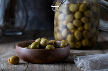 Green olives in a wooden bowl and glass jar