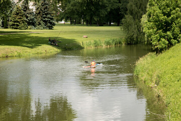 Minsk, Belarus - June 30, 2022 boy in a kayak is swimming along the river, and fishermen are...