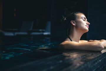 Attractive young woman in a black swimsuit is relaxing in the pool.