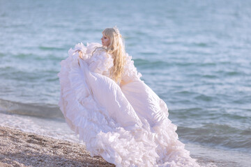Young brunette woman in summer white dress standing on beach and looking to the sea.