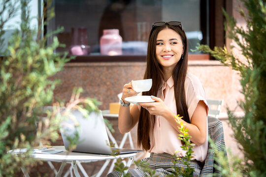 Remote work outside the office, outdoor workplace. Beautiful young asian woman taking rest from the work with a cup of coffee. Autumn mood. Infusion into the business process after summer holidays.
