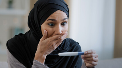 Joyful islamic young woman in hijab smiling happily holding pregnancy test excited pregnant lady...