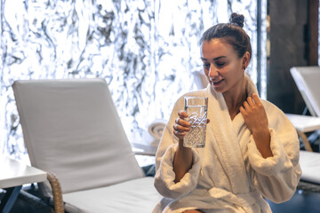 A young woman with a glass of water after the sauna is resting.
