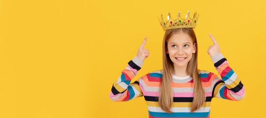 happy teen kid point finger on queen crown on yellow background. Child queen princess in crown horizontal poster design. Banner header, copy space.