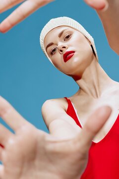 A spectacular young woman in a swimming cap blows a kiss and spreads her hands in front of the camera on a blue background. Take a picture of me concept