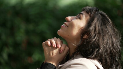 Hopeful woman praying to God standing outside looking at sky. Girl closing eyes in meditation....