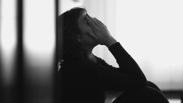 Monochromatic shot of desperate young woman suffering from emotional pain sitting on floor at home