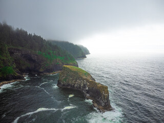 Beautiful seascape. A large stone boulder in the ocean, foamy waves crashing against the stone. Green hilly coast. Overcast weather. Ecology, environmental protection, tourism.