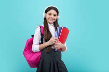 Back to school. Schoolgirl student in headphones with school bag backpack hold book on isolated studio background. School and education concept.