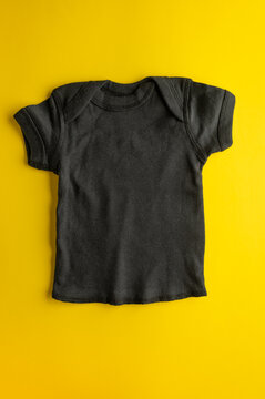 Mockup of a children's black t-shirt for boys and girls on a bright yellow background. Flat lay mockup of cotton sportswear for logos, prints. Close-up.