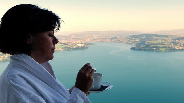 Woman with Bathrobe Drinking a Coffee and Enjoy the View From Balcony with Mountain and Lake View in a Sunny Summer Day on Lake Lucerne From Burgenstock, Nidwalden, Switzerland.