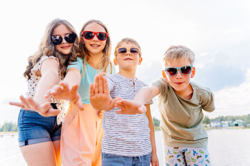 Four children in eyeglasses giving high five at camera in the beach outdoor. Teenager girls with...