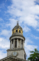 Fototapeta na wymiar London, Great Britain - July 3, 2022: Closeup of clock tower with golden caryatid statues of St. Marylebone Parish Church under blue cloudscape. Green foliage 