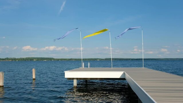 Blue and Yellow Flags fly on the end of a grey pier during a sunny day on Seneca Lake, New York State, USA 