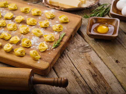 Cooking homemade ravioli, dumplings. Small ravioli, dumplings on a cutting board, kitchen utensils on a wooden background. There are no people in the photo. There is free space to insert.