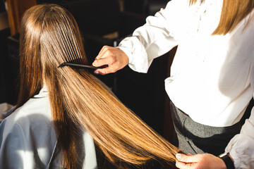 Fototapeta premium Close-up hairdresser combs the girl's hair by styling in a beauty salon.