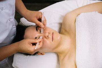 Obraz na płótnie Canvas Woman receiving facial massage with gua sha tool in beauty salon. Beauty and skincare concept with a beautiful woman. Middle aged female using guasha. Massage for facial lifting