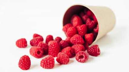 Fresh red raspberries in a paper cup on a white table background