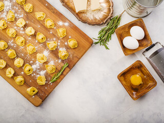 Raw homemade dumplings on a wooden cutting board, ingredients and kitchen utensils on a white...