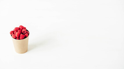 Fresh red raspberries in a paper cup on a white table background