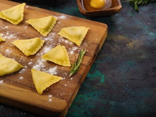 Homemade Italian ravioli on a wooden cutting board, kitchen utensils and ingredients for cooking on a marble background. Recipes of Italian cuisine.