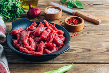 Raw uncooked beef meat sliced in strips with Ingredients for beef stroganoff over rustic wooden background.