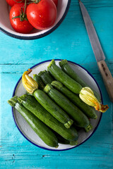 Fresh green zucchinis on a white rustic plate on a blue wooden background. Top view.